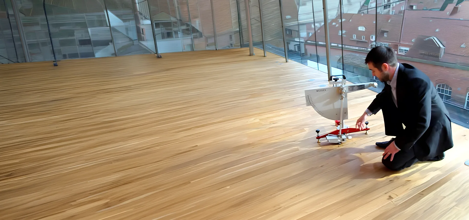 Consultant kneeling to set up a wet pendulum slip tester on a timber floor in a glass walled building